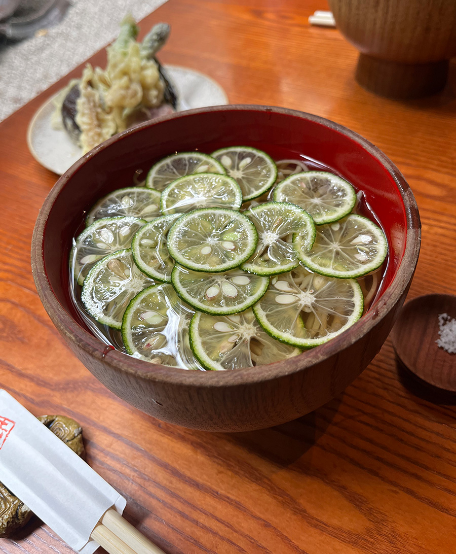 A bowl of sudachi soba noodles with a layer of thinly sliced limes sitting on top